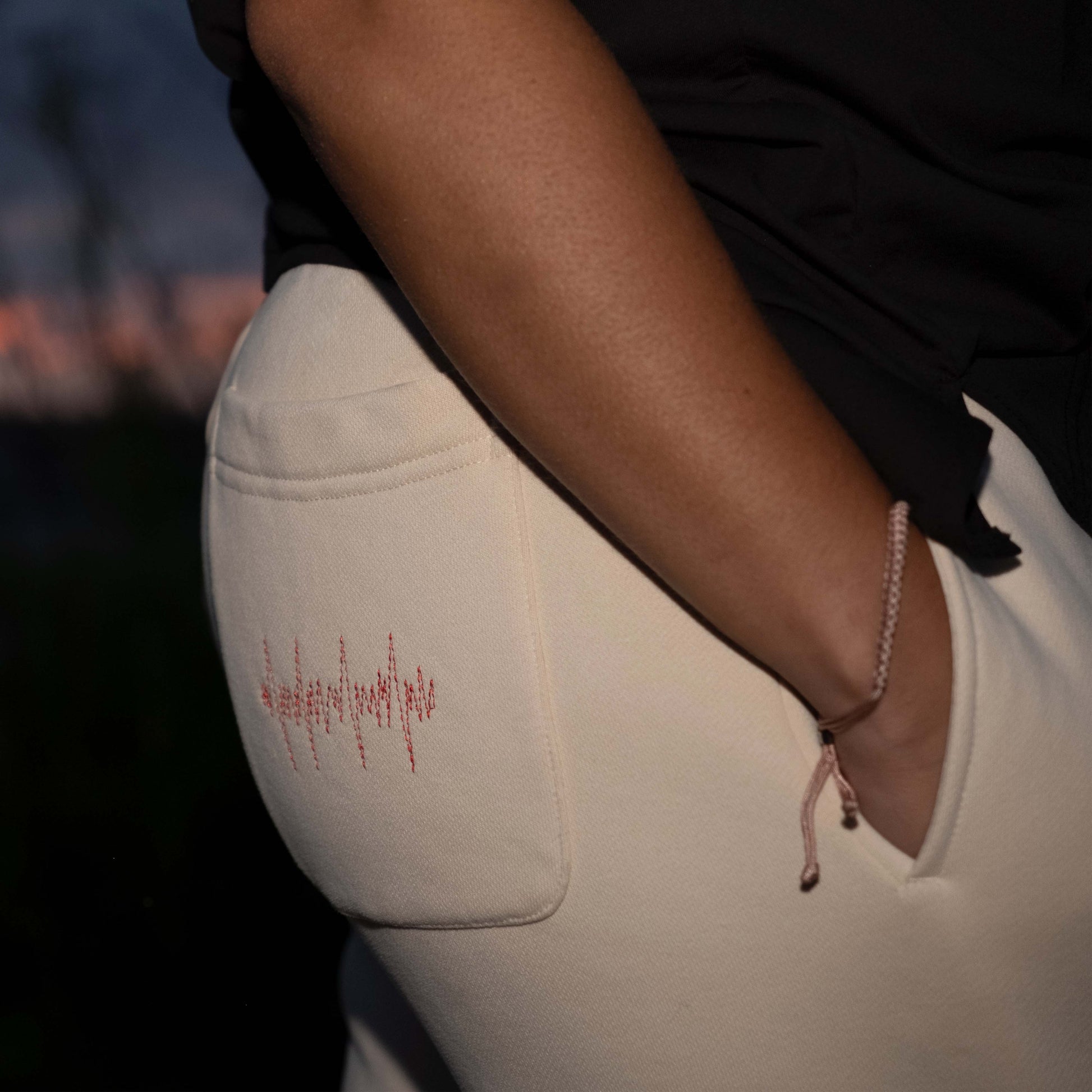 Female model wearing tan Hopesbrands Big Heart sweatpants, featuring red lifeline stitches on the back left pocket. A stylish, comfortable design for casual wear.