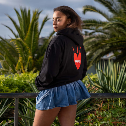 Female model wearing black Big Heart hooded sweatshirt from Hopesbrands, set against a beach backdrop.