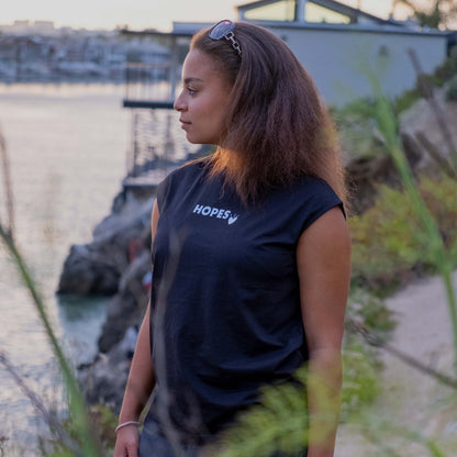 Female model wearing Hopesbrands black Cool Touch tank top with flocked Hopes logo, set against a sunset backdrop.