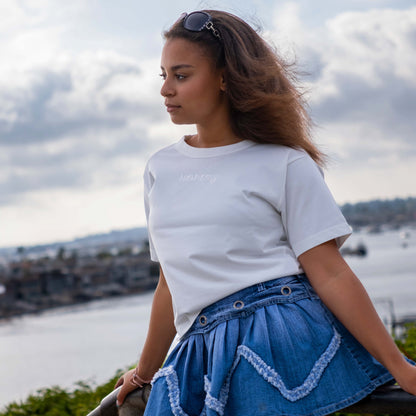 Model wearing an off-white tonal t-shirt from Hopesbrands with an embroidered 'Hopes' logo, standing by the sea. The casual, unisex fit highlights the t-shirt's durability and timeless design, perfect for everyday wear.