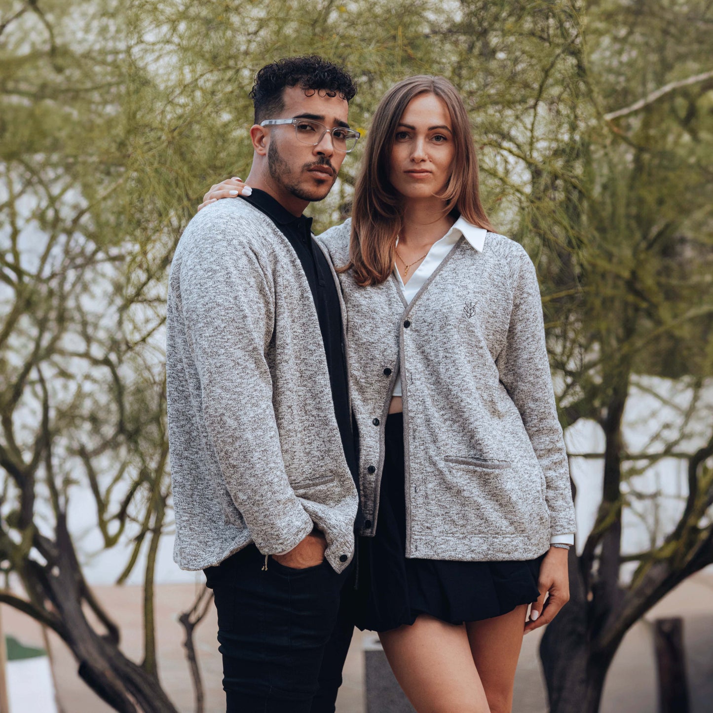 Male and female models wearing Hopesbrands x Tieasy mix charcoal cardigan in a lifestyle shot with a tree backdrop.