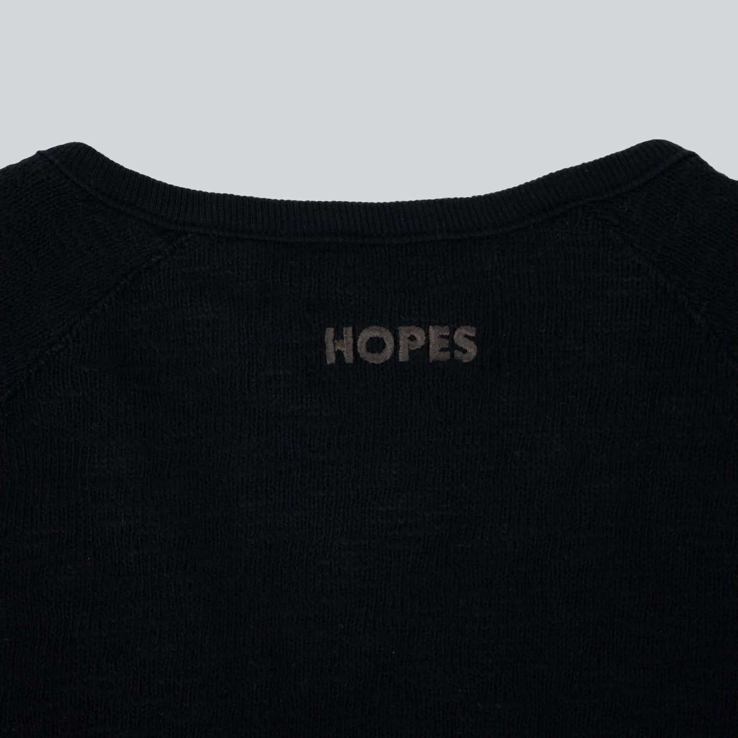 Close-up of tone-on-tone Hopes logo embroidered on black Hopes x Tieasy cardigan, highlighting craftsmanship and style.